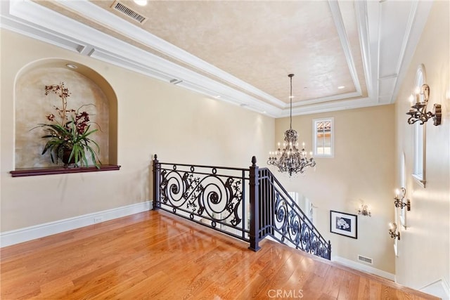 interior space with a tray ceiling, an inviting chandelier, visible vents, and wood finished floors