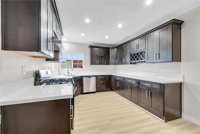 kitchen featuring appliances with stainless steel finishes, dark brown cabinets, light wood finished floors, a sink, and recessed lighting