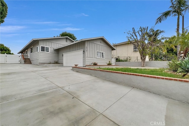 view of front facade featuring board and batten siding, concrete driveway, an attached garage, and fence
