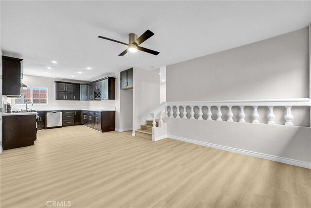 unfurnished living room with light wood finished floors, a ceiling fan, baseboards, stairway, and a sink