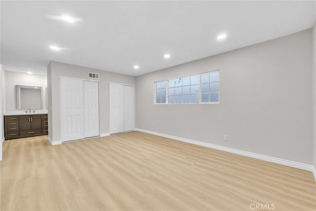 unfurnished bedroom featuring multiple closets, baseboards, a sink, light wood-style flooring, and recessed lighting