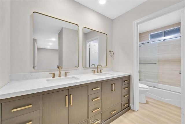full bathroom featuring double vanity, toilet, wood finished floors, and bath / shower combo with glass door