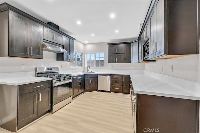 kitchen with stainless steel appliances, under cabinet range hood, a sink, light wood-style floors, and recessed lighting