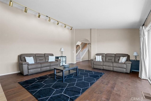 living room with arched walkways, rail lighting, wood finished floors, baseboards, and stairs