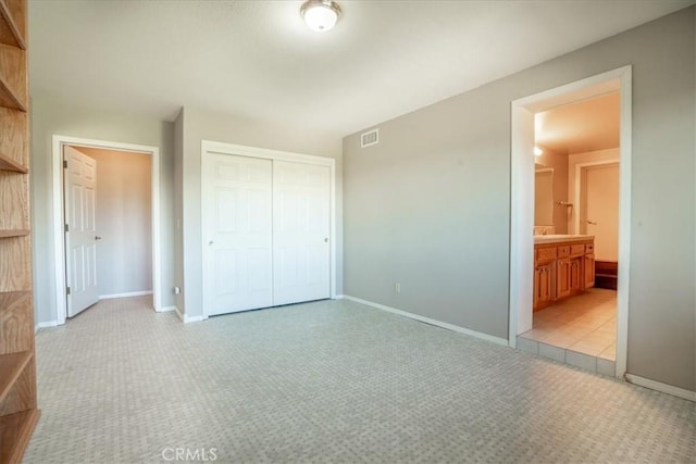 unfurnished bedroom with light colored carpet, a closet, baseboards, and ensuite bath