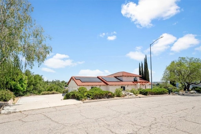 view of front facade featuring roof mounted solar panels, stucco siding, a tiled roof, a garage, and driveway