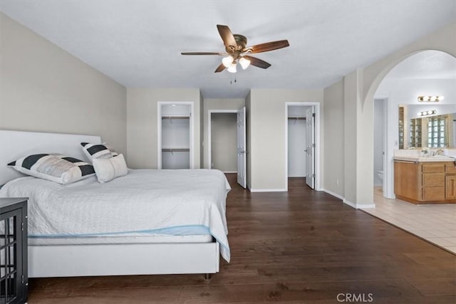 bedroom featuring arched walkways, wood finished floors, a sink, ensuite bath, and baseboards