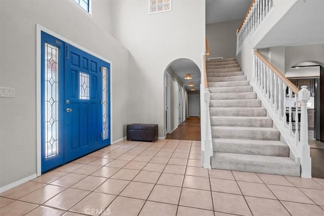 entrance foyer featuring arched walkways, a high ceiling, stairs, light tile patterned floors, and baseboards