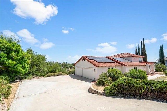 view of side of home with a tiled roof, solar panels, a garage, driveway, and stucco siding