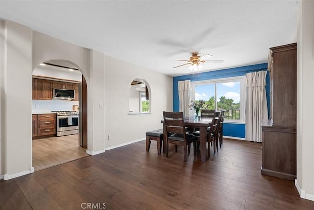 dining room featuring arched walkways, a ceiling fan, dark wood-type flooring, and baseboards