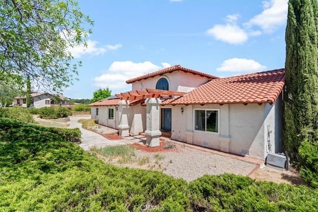rear view of property with stucco siding, a pergola, and a tile roof