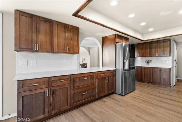 kitchen with stainless steel fridge with ice dispenser, light wood-style flooring, backsplash, light countertops, and recessed lighting