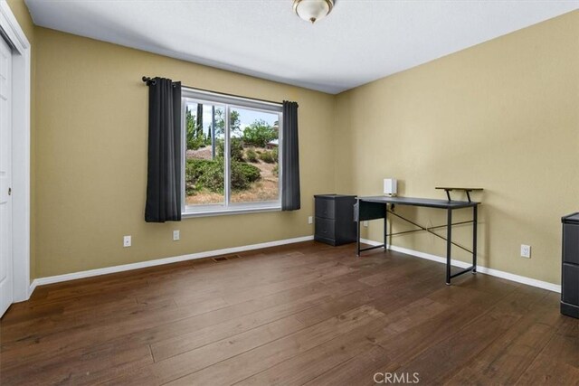 unfurnished office with dark wood-style flooring and baseboards