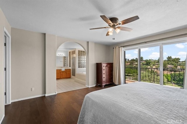bedroom with access to outside, arched walkways, hardwood / wood-style flooring, baseboards, and ensuite bathroom