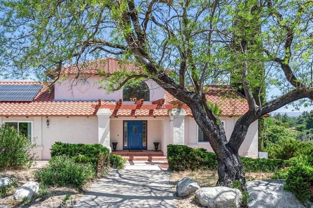 mediterranean / spanish-style home featuring stucco siding, a tiled roof, and roof mounted solar panels
