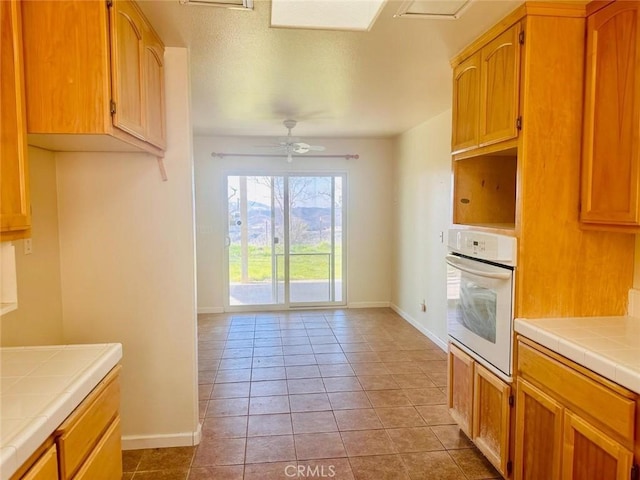 kitchen featuring ceiling fan, white oven, tile counters, light tile patterned floors, and baseboards