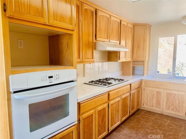 kitchen with dark tile patterned flooring, tile counters, white appliances, under cabinet range hood, and decorative backsplash
