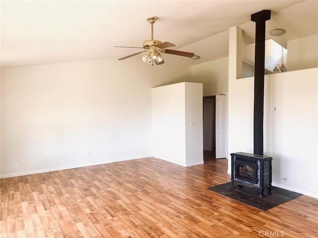 unfurnished living room featuring a wood stove, light wood finished floors, baseboards, and ceiling fan