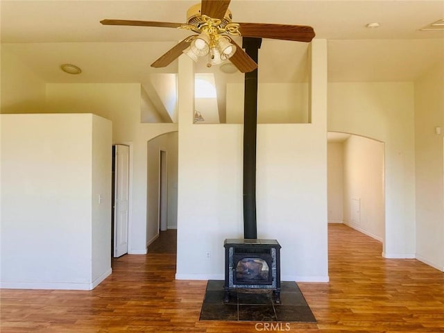 unfurnished living room featuring a wood stove, baseboards, wood finished floors, and a ceiling fan