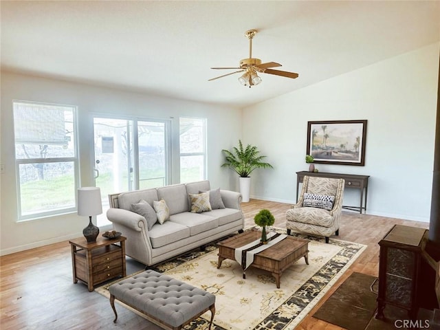 living room featuring a ceiling fan, baseboards, light wood finished floors, and vaulted ceiling