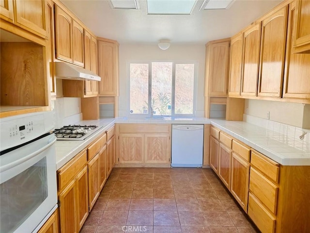 kitchen featuring white appliances, light brown cabinets, tile countertops, and under cabinet range hood
