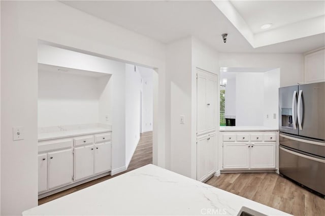 kitchen featuring stainless steel fridge with ice dispenser, white cabinets, light wood-type flooring, and light stone countertops