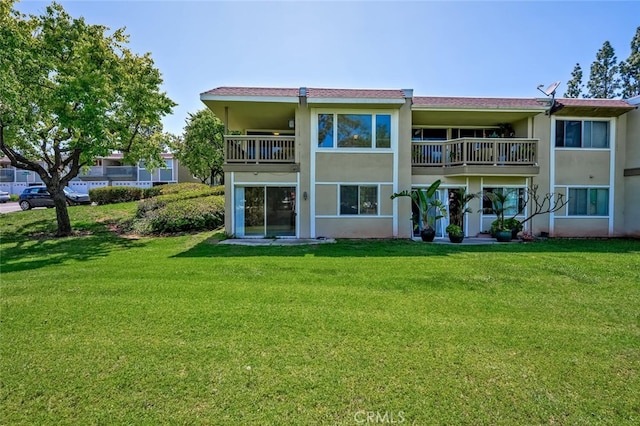 back of property featuring stucco siding, a lawn, and a balcony