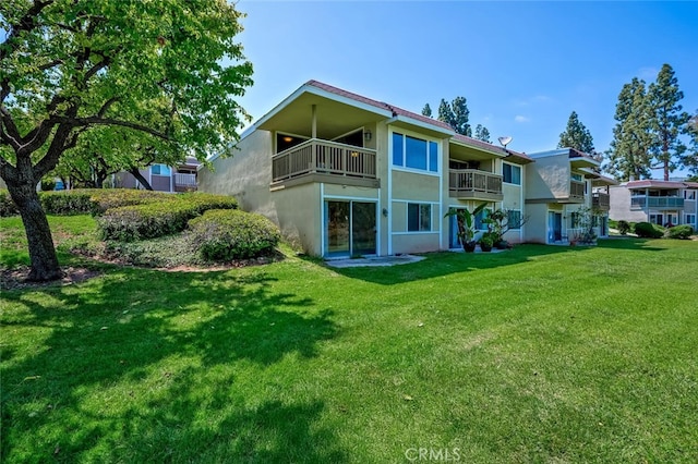 rear view of property with a lawn, stucco siding, and a balcony