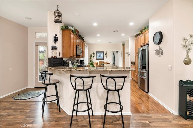 kitchen with a peninsula, light wood-style floors, stainless steel appliances, and a kitchen bar