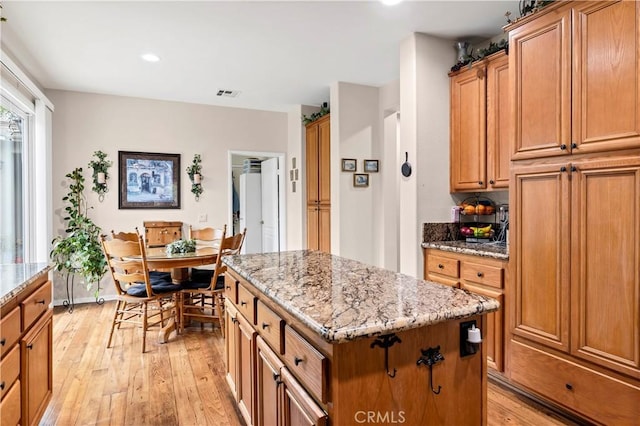 kitchen featuring a center island, brown cabinetry, light stone counters, light wood finished floors, and visible vents