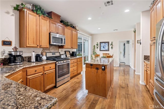 kitchen with stone countertops, appliances with stainless steel finishes, visible vents, a kitchen island, and light wood-type flooring