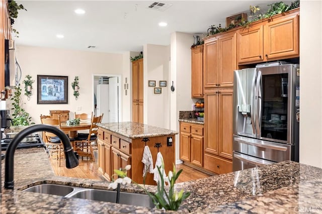 kitchen with light wood finished floors, dark stone countertops, a sink, stainless steel refrigerator with ice dispenser, and visible vents
