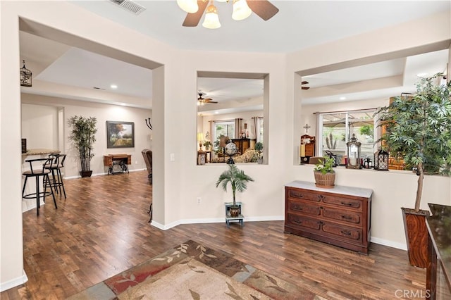 interior space with a raised ceiling, a ceiling fan, visible vents, and wood finished floors