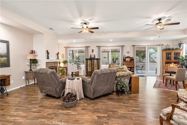 living room with visible vents, wood finished floors, a ceiling fan, and a warm lit fireplace