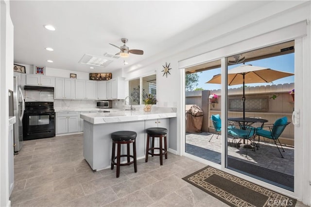 kitchen featuring a peninsula, a breakfast bar area, under cabinet range hood, ceiling fan, and appliances with stainless steel finishes