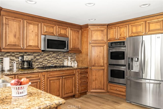9492 Brynmar Dr, Villa Park, CA 92861 - kitchen featuring appliances with stainless steel finishes, brown cabinetry, light stone counters, backsplash, and light wood finished floors