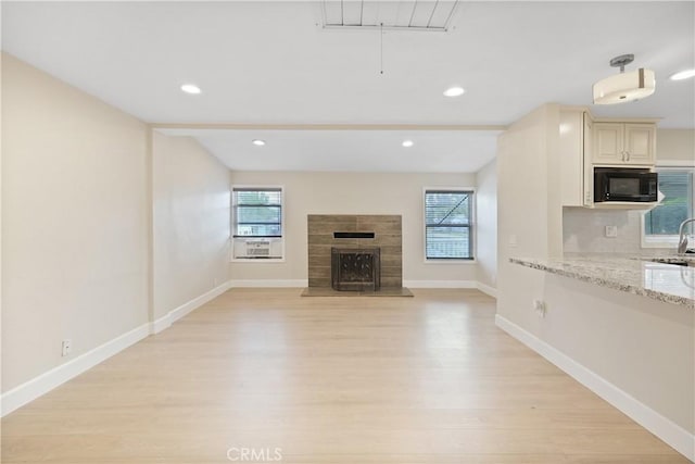 23821 Norma Dr, Menifee, CA 92587 - unfurnished living room with plenty of natural light, light wood finished floors, a fireplace with raised hearth, baseboards, and recessed lighting