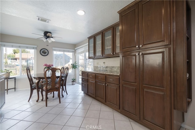 kitchen featuring light tile patterned floors, a ceiling fan, a textured ceiling, visible vents, and baseboards