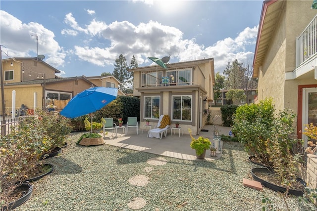 rear view of house with fence, a patio, stucco siding, and a balcony