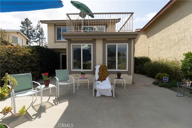 back of property with board and batten siding, a patio area, stucco siding, and a balcony