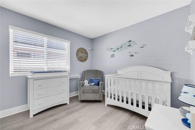bedroom with light wood finished floors, baseboards, and a crib