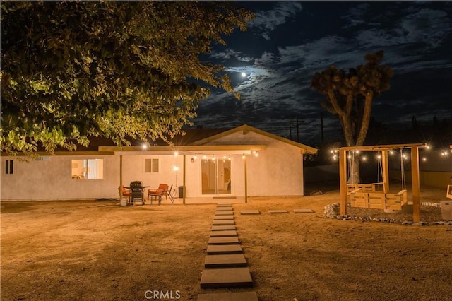 back of house at night featuring stucco siding and a patio area