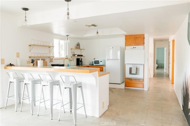 kitchen with white appliances, a breakfast bar, a peninsula, hanging light fixtures, and light countertops