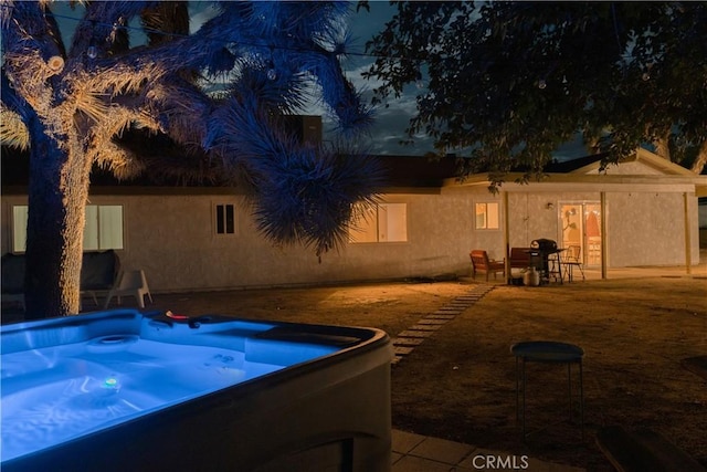 rear view of property featuring a hot tub, a patio area, and stucco siding