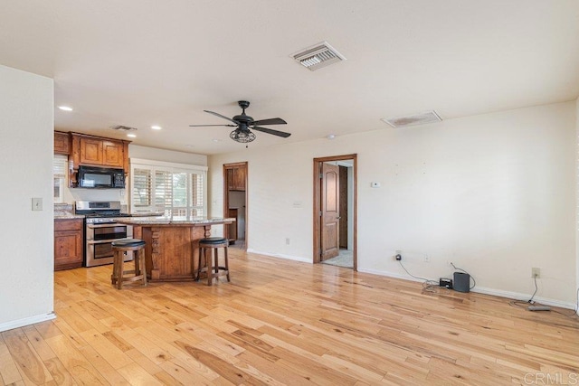 kitchen with a breakfast bar area, visible vents, black microwave, double oven range, and light wood-style floors
