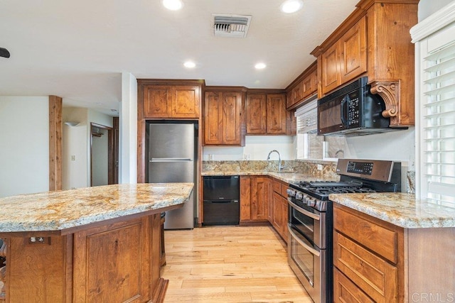 kitchen with light wood-style floors, visible vents, brown cabinetry, and black appliances