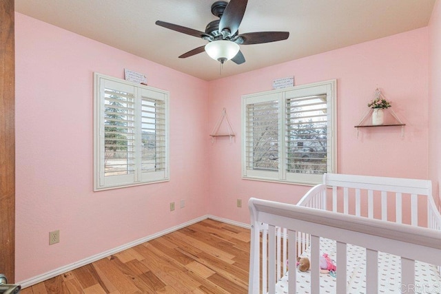 bedroom with ceiling fan, a nursery area, light wood-type flooring, and baseboards