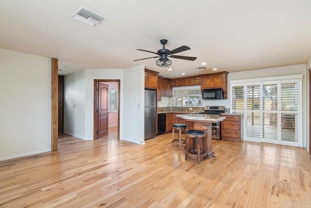 kitchen featuring a breakfast bar area, brown cabinetry, visible vents, black appliances, and light countertops