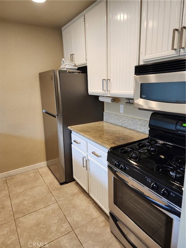 kitchen featuring light tile patterned flooring, white cabinets, light stone countertops, baseboards, and appliances with stainless steel finishes