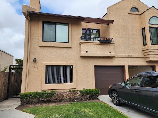 townhome / multi-family property with a balcony, driveway, fence, a garage, and stucco siding
